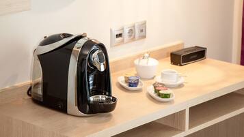 A modern hotel room with a coffee maker, a mirror, a hanging light fixture, and a small table with a teapot and cups.