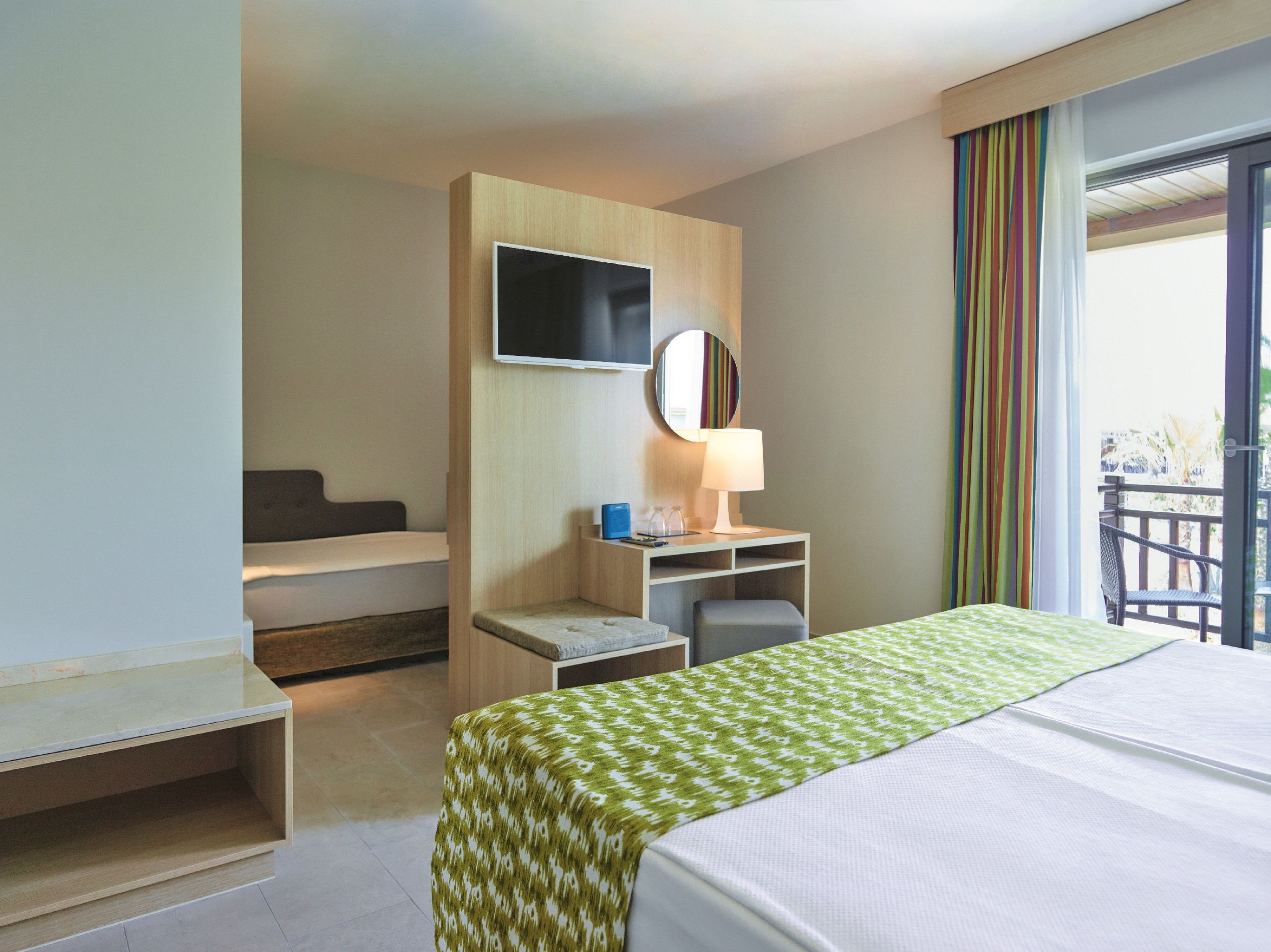 Une chambre d’hôtel comprenant un lit, un bureau avec une chaise, un téléviseur fixé au mur et un balcon avec vue.