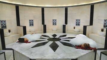 A circular hot tub with a marble floor and black accents, surrounded by tiled walls with decorative patterns.