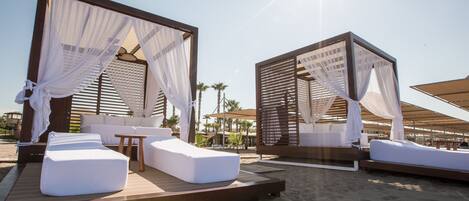 A beachside resort with two canopy beds, wooden deck, and outdoor seating area.