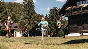 Children play in a family-friendly outdoor space surrounded by a well-maintained lawn and evergreen trees.