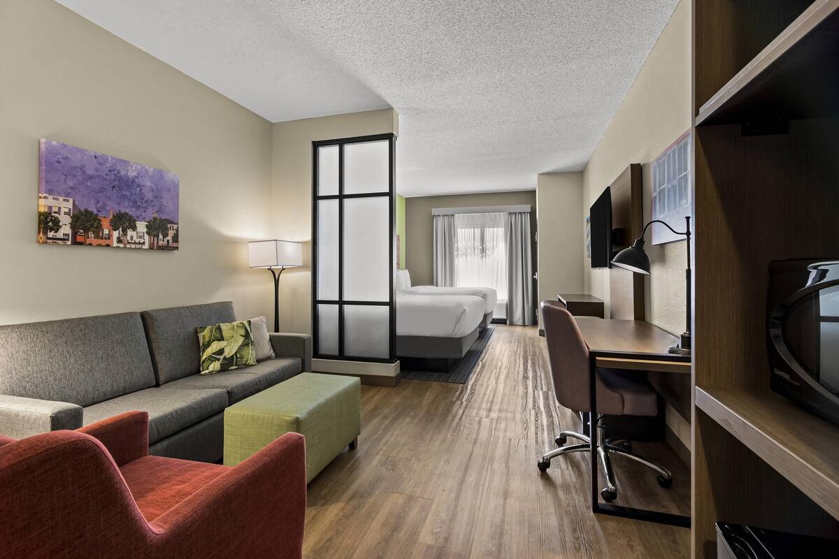 Une chambre d’hôtel équipée d’un canapé, d’un bureau, d’une chaise, d’un lit, d’une télévision et d’un tableau au mur.