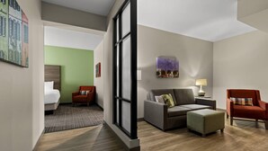 A hotel room with a bed, a sofa, a chair, a small table with a lamp, and a painting on the wall. - Comfort Suites Charleston West Ashley (Charleston)
