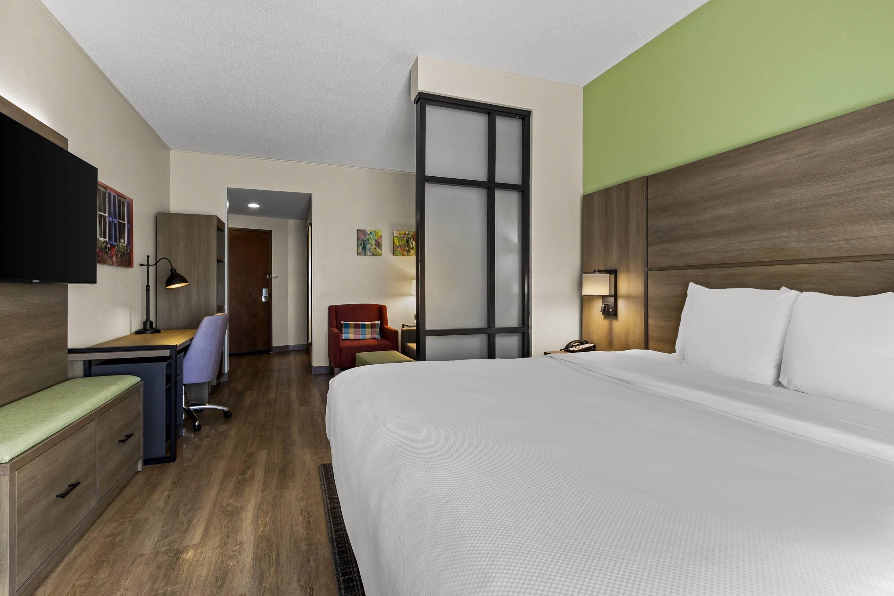 A hotel room with a large bed, a desk, a chair, and a TV.