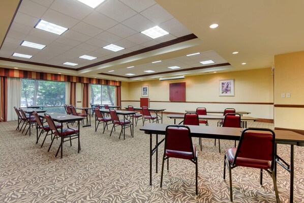 Une salle de conférence équipée de tables et de chaises, dotée d’un sol recouvert de moquette et d’un éclairage au plafond.