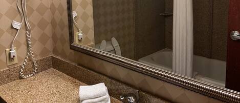 Baño con encimera de granito, lavamanos, espejo, secador de pelo y cortina de ducha.