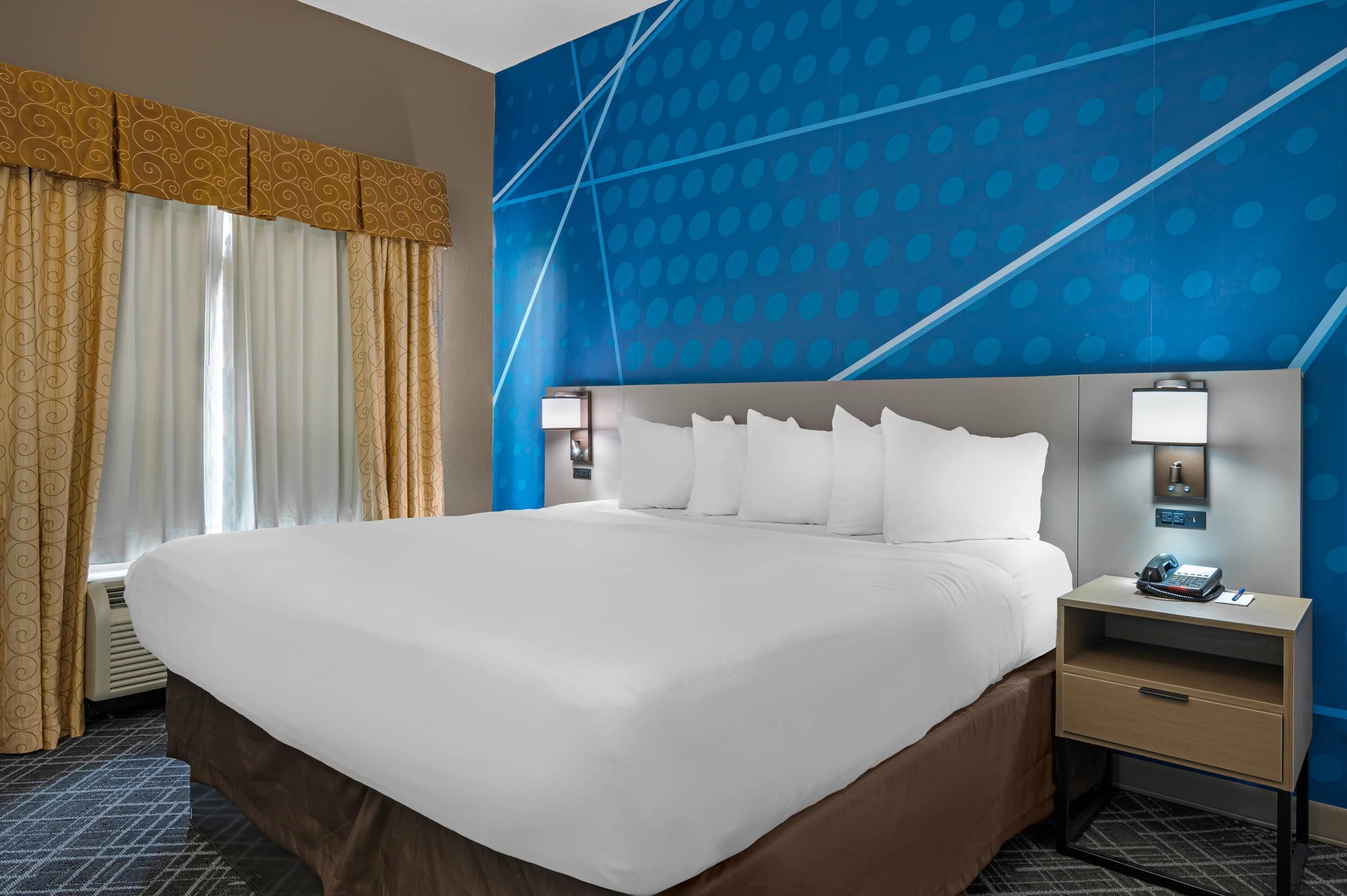 A hotel room with a large bed, a nightstand with a lamp, and a wall with a geometric pattern.