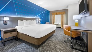 Une chambre d’hôtel avec un lit, un bureau, une chaise, une télévision et une moquette à motifs.