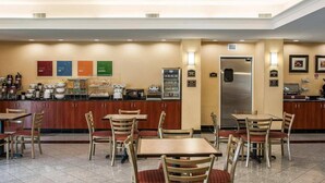 Un espace pour le petit-déjeuner à l’hôtel, avec un buffet, des tables et des chaises, ainsi qu’un réfrigérateur.