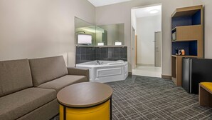 Une chambre d’hôtel avec un canapé, une table ronde, une baignoire, un miroir et un réfrigérateur.
