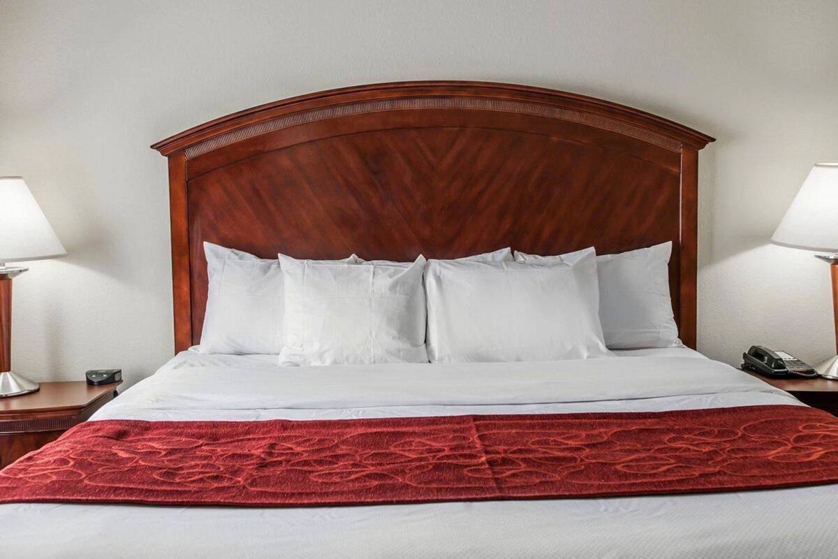 Ein Hotelzimmer mit einem großen Bett, zwei Nachttischen, einer roten Tagesdecke und einem hölzernen Kopfteil.