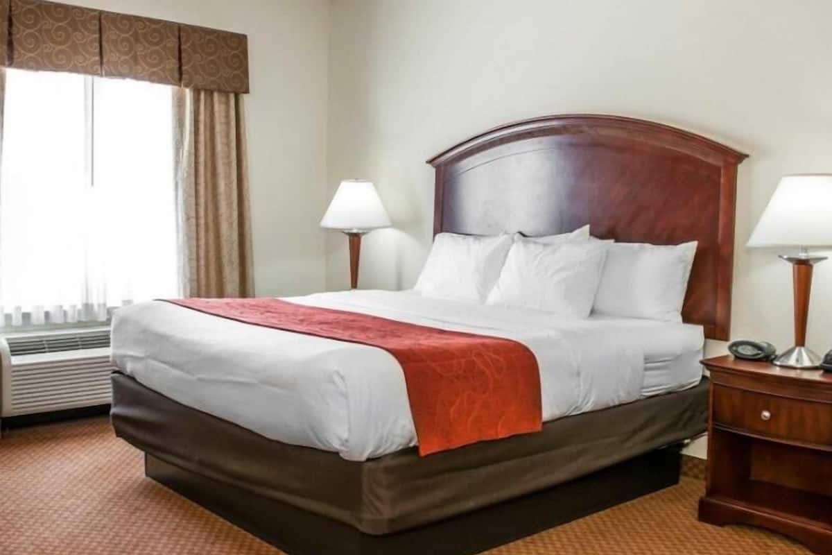 Ein Hotelzimmer mit einem großen Bett, zwei Nachttischlampen, einem Holz-Kopfteil und einem Fenster mit Vorhängen.
