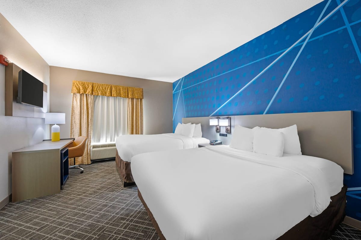 Ein Hotelzimmer mit zwei Betten, einem Schreibtisch, einem Sessel, einem Fernseher und einer blauen Wand.