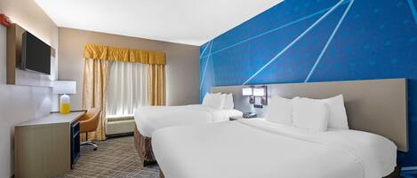 A hotel room with two beds, a desk, a chair, a TV, and a large blue wall.