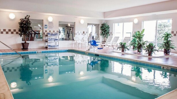 Une piscine intérieure dotée de chaises longues, de plantes en pot et d’un espace de réception bien visible.