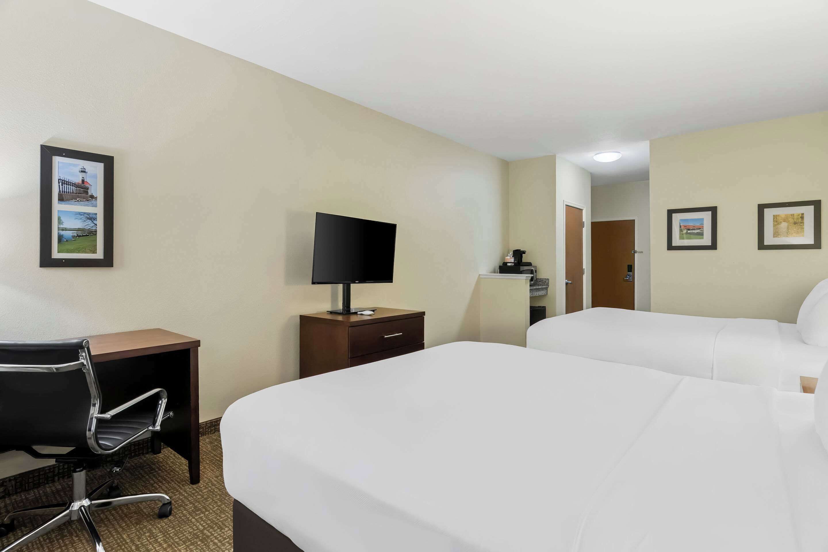 A hotel room with two beds, a desk with a chair, a TV, and a small cabinet.