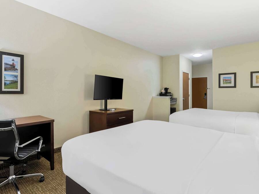 A hotel room with two beds, a desk with a chair, a TV, and a small cabinet.