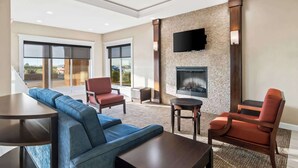 A modern living room with a fireplace, a large TV mounted on the wall, and a seating area with a blue sofa and two chairs. - Comfort Inn Hebron-Lowell Area (Hebron)