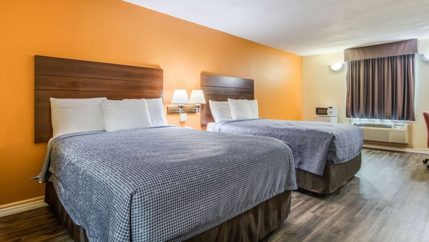 Een hotelkamer met twee bedden, houten hoofdeinden en een raam met gordijnen.