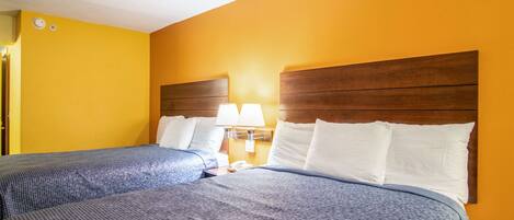 Ein Hotelzimmer mit zwei Betten, einem hölzernen Kopfteil, einem Nachttisch mit Lampe und einem an der Wand befestigten Telefon.