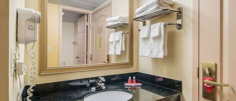 Un baño de hotel con un lavabo negro, un espejo grande, un secador de pelo y un perchero para toallas.