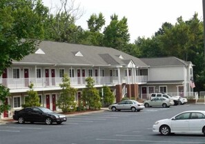 Un motel de dos pisos, con varias habitaciones y un estacionamiento con varios autos.