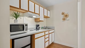 Une cuisine moderne avec des meubles blancs, des éléments décoratifs en bois, un four à micro-ondes, une machine à café et une plante en pot.