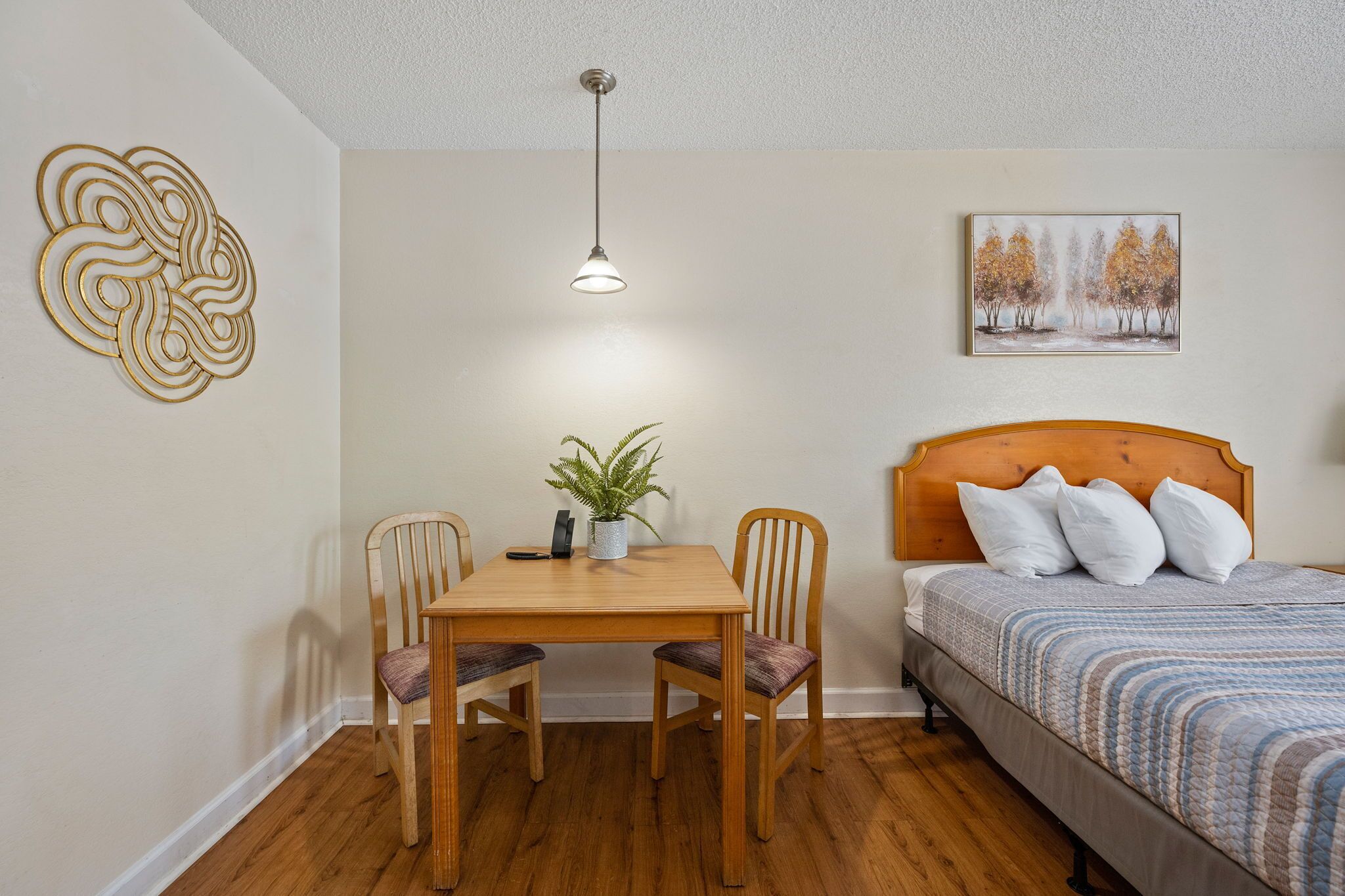 A bedroom with a wooden bed, a bedside table with a plant, and a wall art piece.