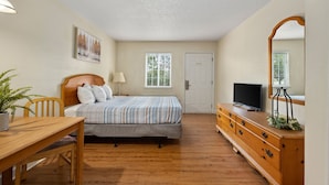 Une chambre à coucher comprenant un lit, une commode, un téléviseur, une fenêtre avec des stores et une porte.