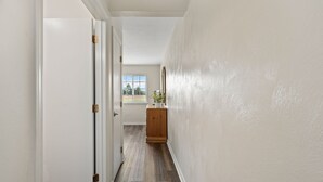 Un couloir aux murs blancs, doté d’un plancher en bois et d’une fenêtre au fond.