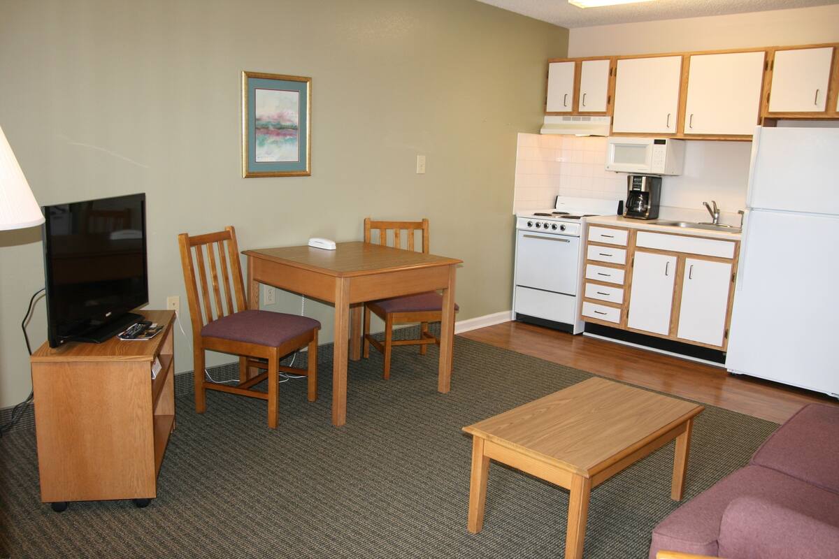 A compact living space with a kitchenette, a dining area with two chairs, a television on a stand, and a sofa.