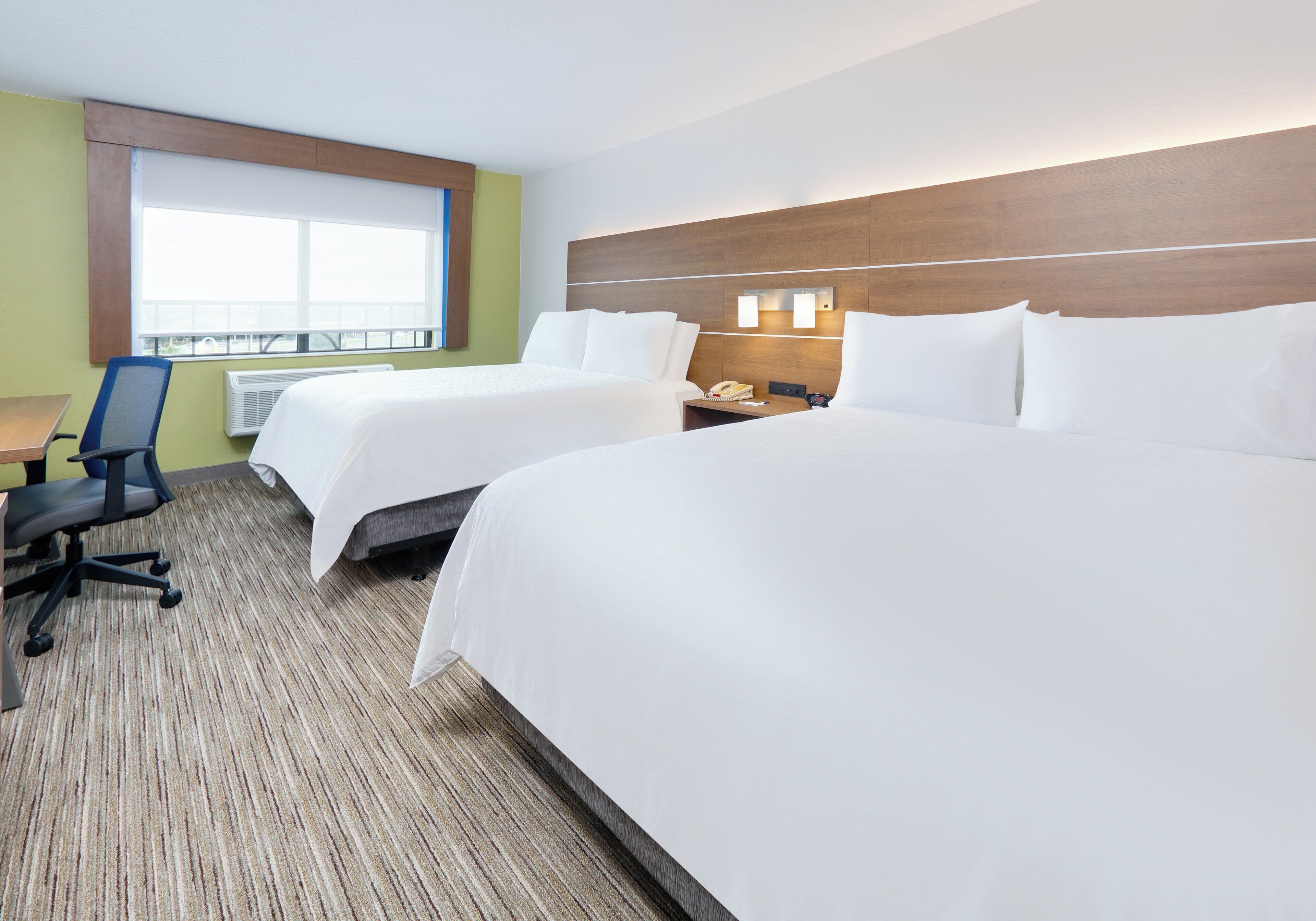 A hotel room with two beds, a desk, a chair, and a window with blinds.