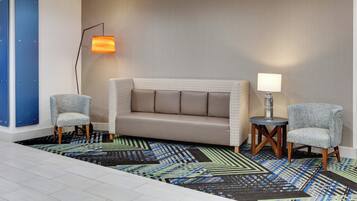 Une chambre d’hôtel avec un canapé, deux fauteuils, un tapis à motifs et une lampe fixée au mur.