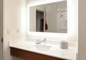Un baño con lavamanos blanco, un espejo y dispensador de toallas.
