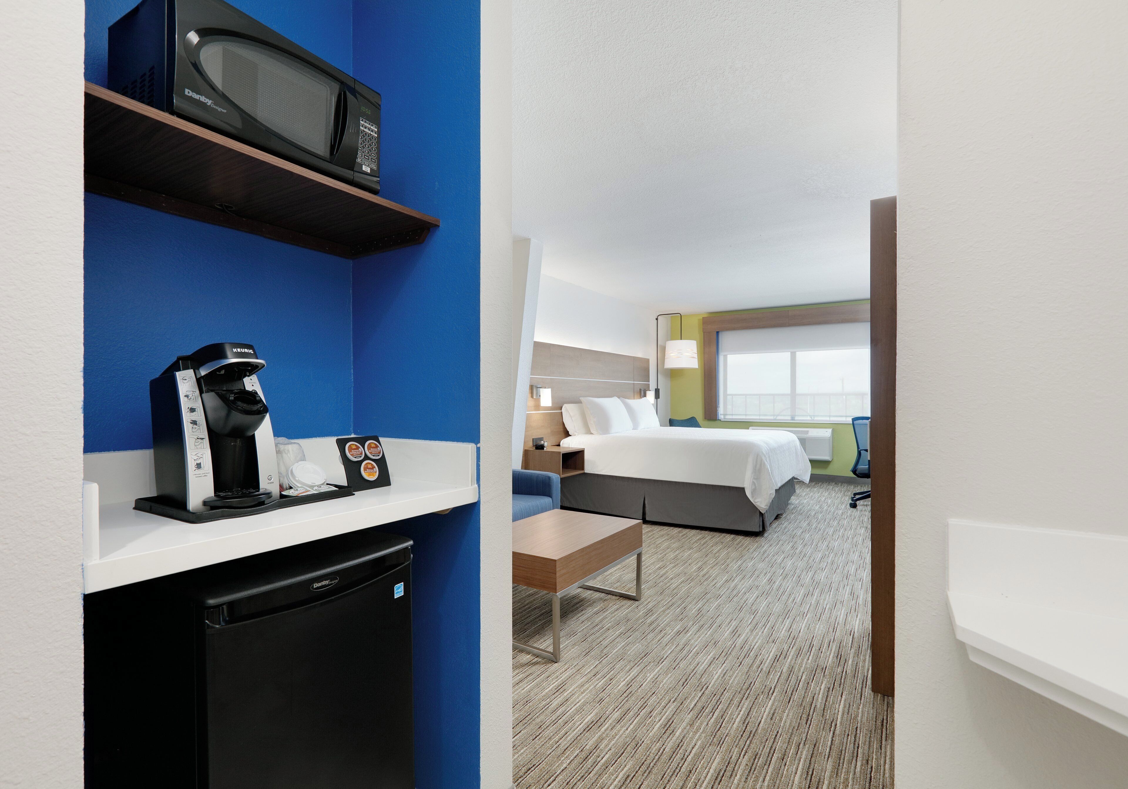 A hotel room with a bed, bedside table, lamp, and a view of the outside.