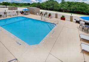 A swimming pool with a surrounding patio area, including chairs and a barbecue grill.
