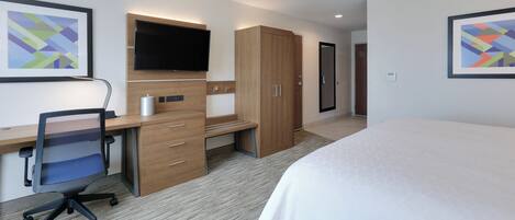A hotel room with a bed, desk, chair, television, wardrobe, and artwork on the walls.