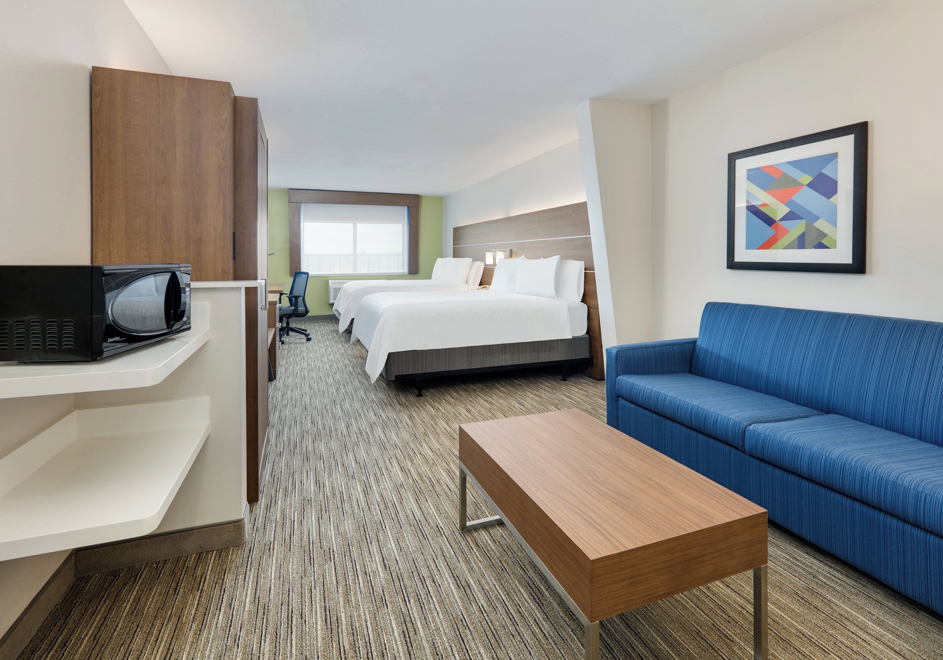 Une chambre d’hôtel avec un lit, un bureau avec un ordinateur, un canapé bleu et une petite table.