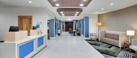 A hotel lobby with a reception desk, seating area, and a TV screen.