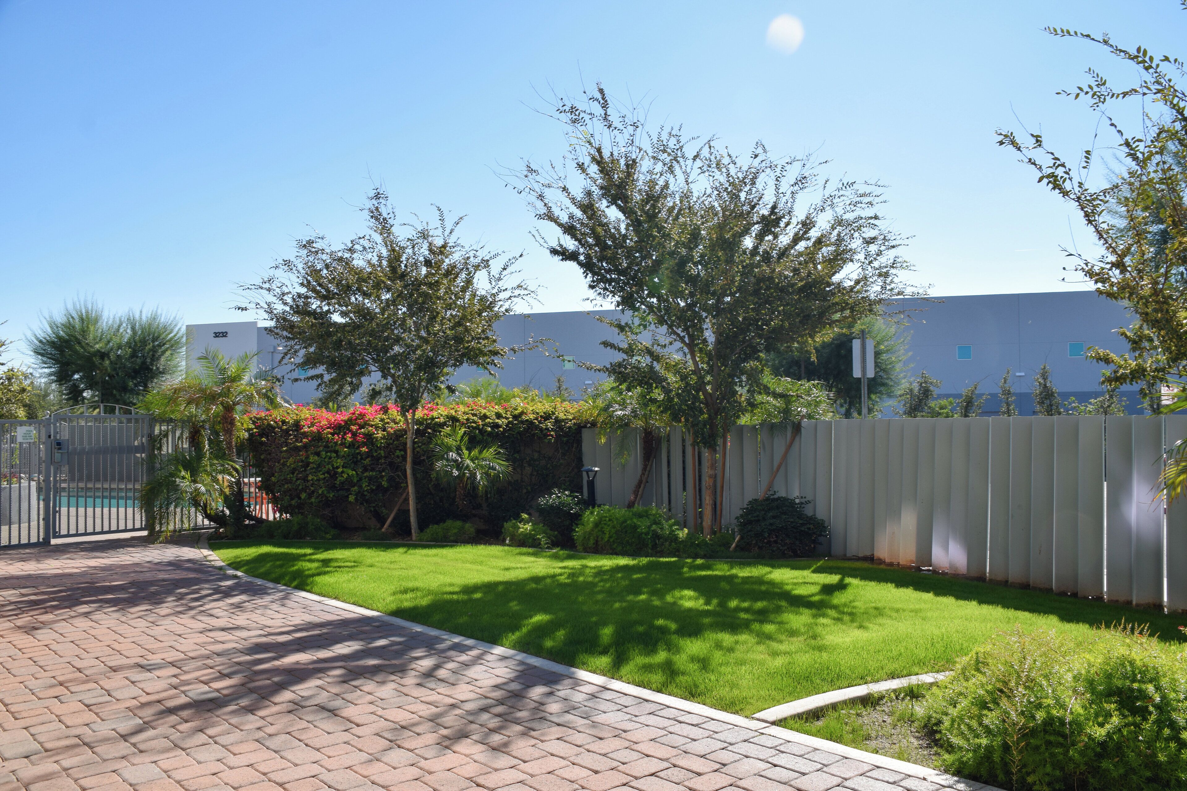 A well-maintained garden with a paved walkway, a white fence, and a building in the background.