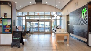 A modern hotel lobby with a reception desk, seating area, and large glass doors leading outside. - Holiday Inn Hotel & Suites PHOENIX AIRPORT by IHG (Phoenix)