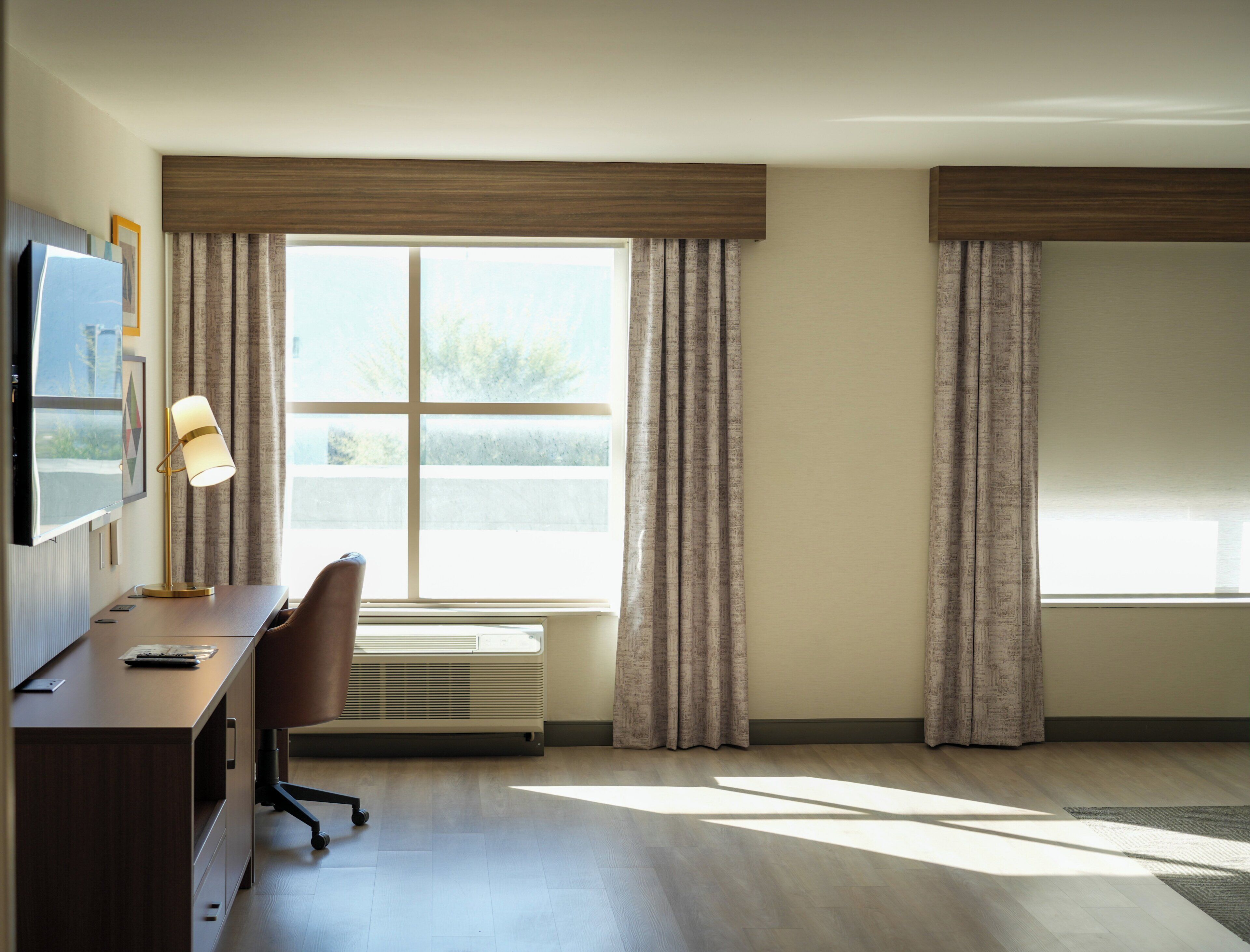 Habitación de hotel con escritorio, silla y un amplio ventanal con cortinas.