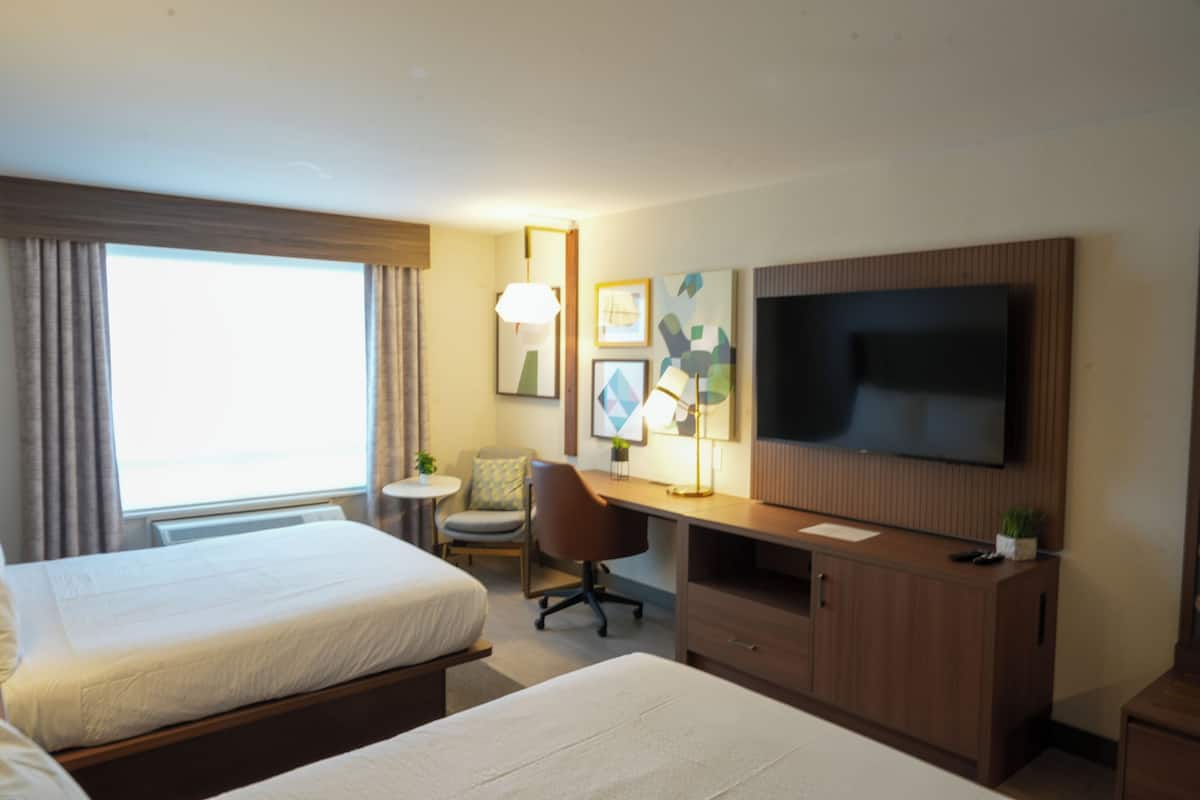 A hotel room with two beds, a desk, a chair, a TV, and a window with curtains.