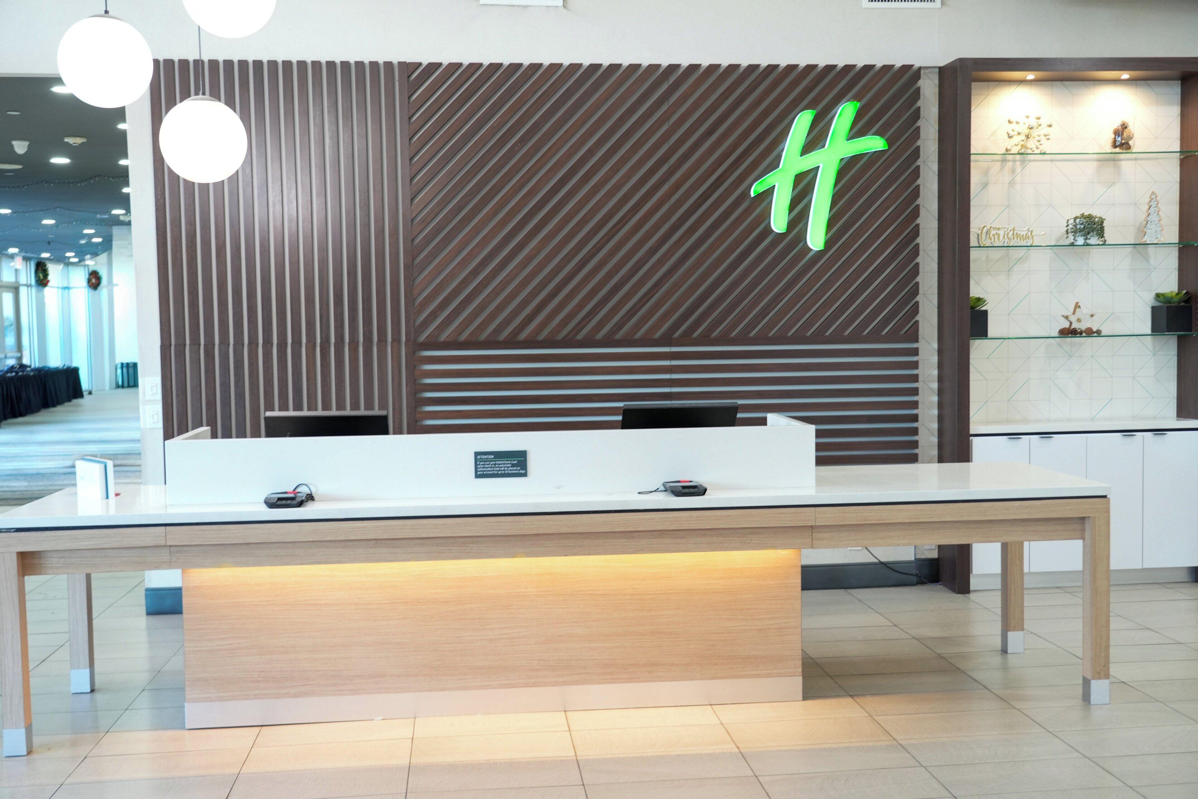 A reception desk with a modern design, a green 'H' logo, and a small sign indicating a 24-hour service area.