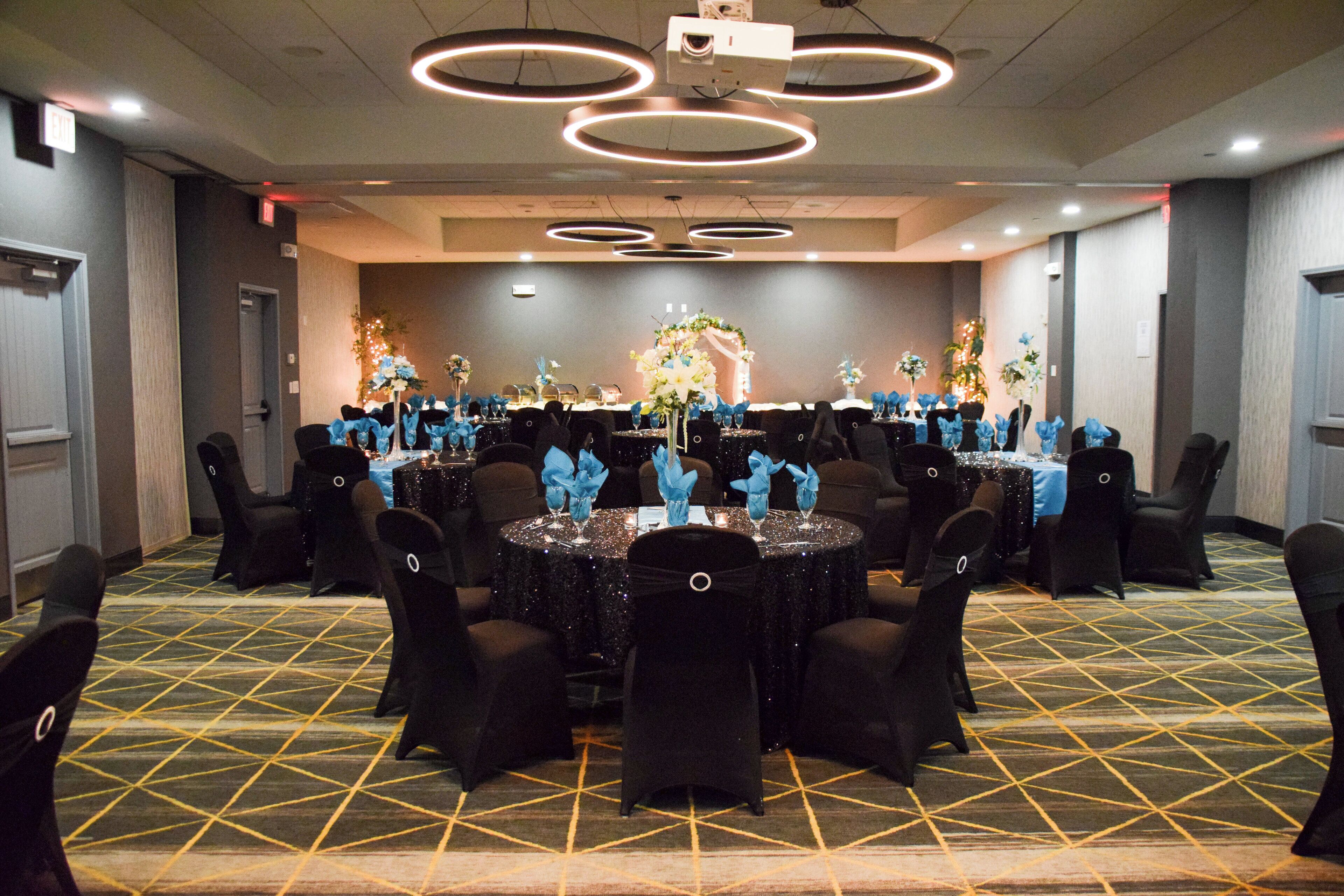 A banquet hall with round tables, black chairs, and a floral centerpiece.