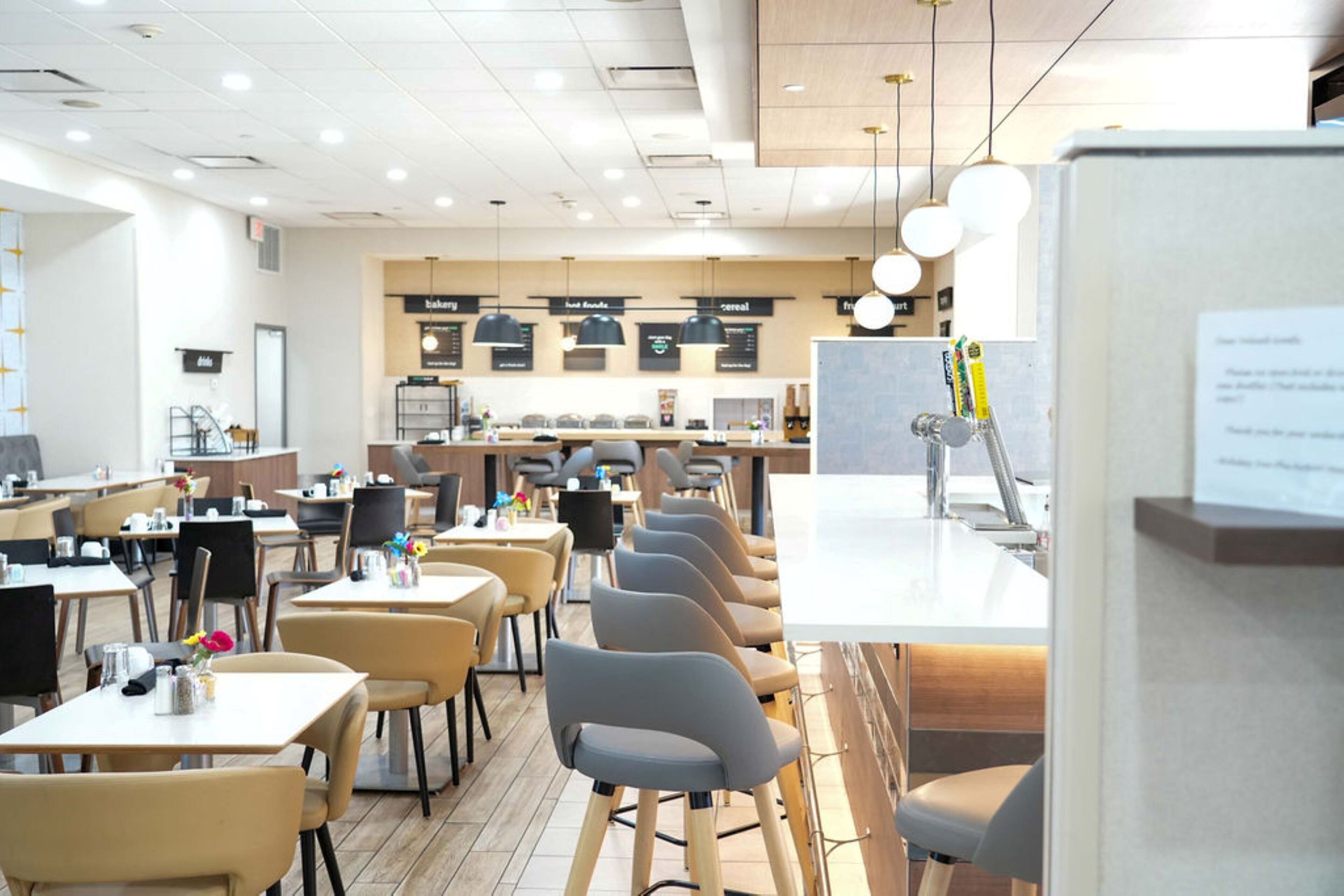 A modern cafe with multiple seating areas, including tables and chairs, and a counter with a menu board in the background.