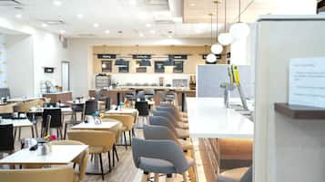 A modern cafe with multiple seating areas, including tables and chairs, and a counter with a menu board in the background.