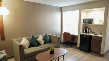 A compact living space with a sofa, a small table, a microwave, and a compact kitchenette.