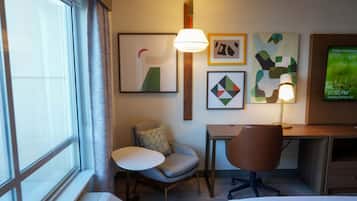 A hotel room with a desk, two chairs, a lamp, and artwork on the wall.