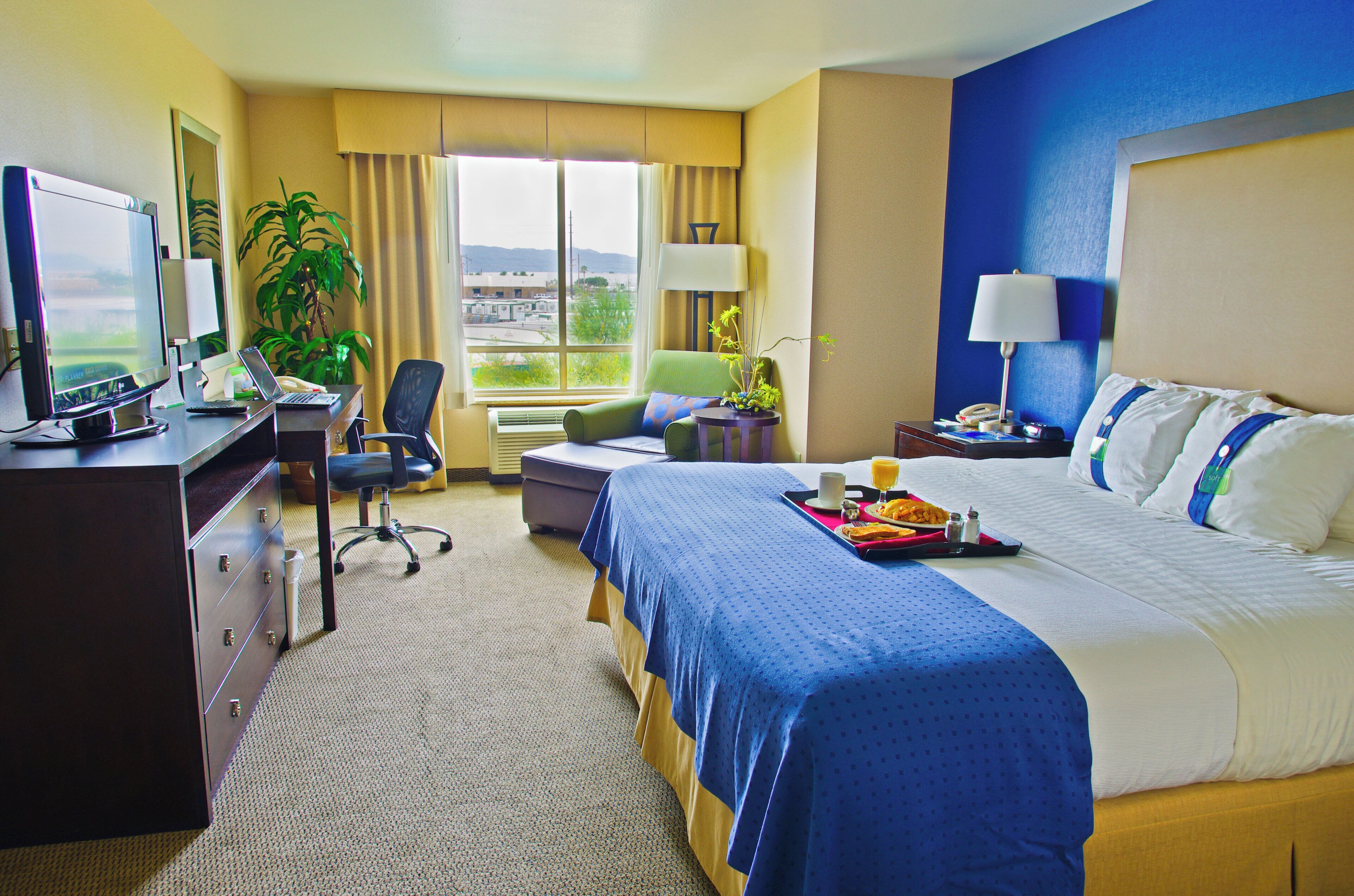 A hotel room with a bed, desk, chair, and a view of the outdoors.